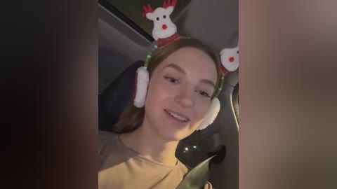 Media: Video of a young woman with light skin, brown hair, and red reindeer headband, wearing headphones, smiling in a car.