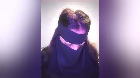 Media: Video of a person wearing a black blindfold, casting purple shadows on their face, against a blurred background.