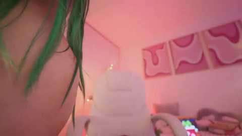 Media: A low-resolution, grainy photo of a young woman with green hair, topless, in a dimly lit room with pink and purple lighting. In the background, a white chair and abstract art on the wall.