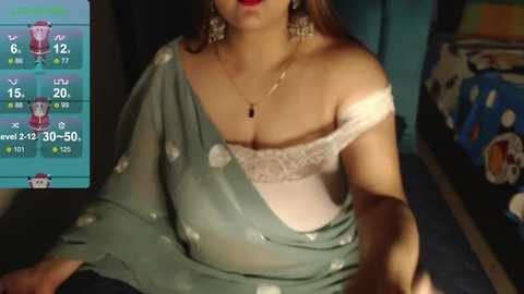 Media: Video of a woman with light brown skin, wearing a green polka-dotted sari with a white lace bra, in a dimly lit room with a weather app screen.