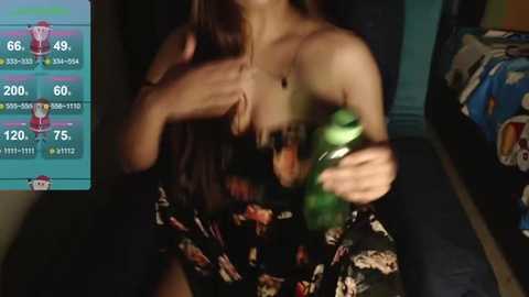 Media: A dimly-lit video of a woman with long brown hair in a black floral dress, holding a green can, against a dark background. A smartphone screen shows a game interface in the left corner.