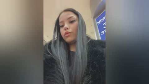 Media: Video of a young woman with long, straight, silver-gray hair, wearing a black fur coat, standing in front of a car's interior with a blue dashboard visible.