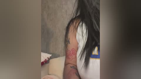 Media: Video of a woman with long black hair and a visible tattoo on her upper arm, wearing a white shirt, leaning over a man lying on a bed.