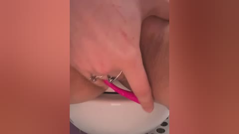 Media: A close-up video of a person with light skin using a pink toothbrush to clean their teeth. The background is a solid, warm peach color. The image focuses on the hand holding the toothbrush and the teeth being brushed.