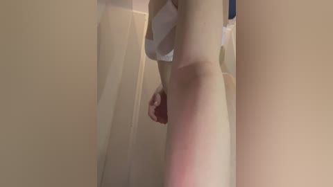 Media: A video of a nude, fair-skinned woman standing in a dimly lit, beige-tiled bathroom, with a visible red mark on her thigh. The focus is on her lower body, with her hand near her genital area.