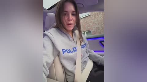 Media: A video of a young woman in a light gray \"POLICE\" hoodie, driving a luxury car with beige leather seats and blue ambient lighting.