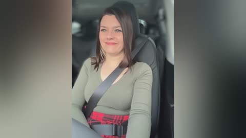 Media: Video of a smiling Caucasian woman with shoulder-length brown hair, wearing a green long-sleeve top and red plaid skirt, seated in a car with a safety belt, looking relaxed.