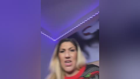 Media: A video shows a blonde woman with fair skin, wearing a red shirt, speaking passionately against a purple-lit ceiling with abstract artwork in the background.