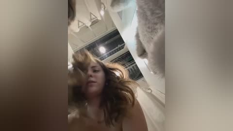 Media: Video of a topless woman with long, wavy hair, captured in a mirror's reflection, showing her from behind. She is in a bathroom with a shower curtain and window visible in the background.