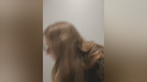 Media: Blurry video of a person with long, wet hair, leaning forward, against a plain, beige background.