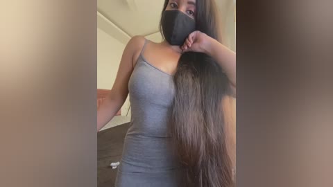 Media: A video of a young South Asian woman with long, straight black hair, wearing a grey tank top, black face mask, and black hairband, taken indoors with blurred background.