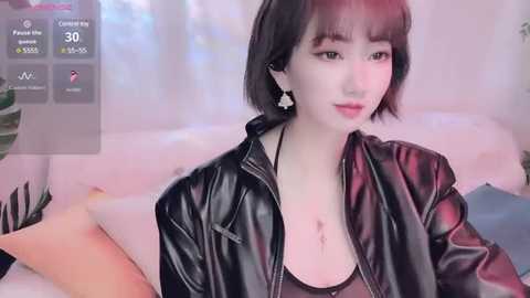 Media: Video of a young Asian woman with short black hair, wearing a black leather jacket, sitting on a couch, looking at a smartphone.