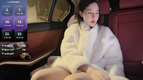 Media: A video of a young Asian woman in a white fur coat, sitting in the backseat of a luxury car with red leather seats.