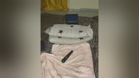 Media: Video of a messy bedroom with a laptop on a bed, a remote control on a pink blanket, and a yellow curtain in the background.