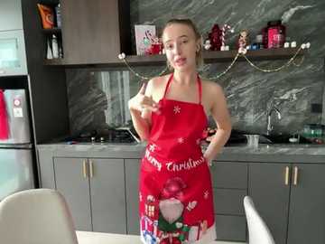 Media: Video of a fair-skinned, blonde woman in a red apron with holiday designs, standing in a modern kitchen with grey marble backsplash, silver appliances, and festive decorations.