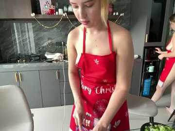 Media: Video of a blonde woman in a red apron with a Christmas design, standing in a modern kitchen with stainless steel appliances and dark countertops.