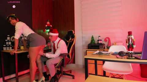 Media: Video of a festive office scene with a woman in a Santa hat leaning over a man in a suit, both seated at desks, surrounded by Christmas decorations.