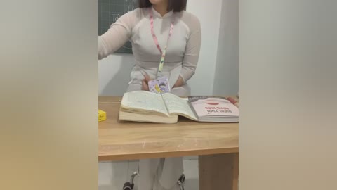 Media: A video of a woman seated at a wooden desk, wearing a white long-sleeved shirt, holding an open book, with a yellow pen and a book titled \"Buddhist Sutras\" beside her.