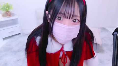 Media: Video of an Asian woman with long black hair, wearing a red dress with a white collar and a pink face mask, kneeling on a white carpet.