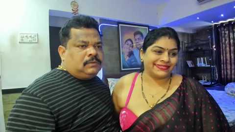 Media: Video of an overweight South Asian couple in a living room; man in striped shirt, woman in pink bra and black sari.