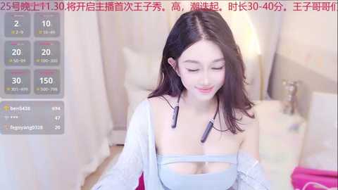 Media: Video of an Asian woman with fair skin, long black hair, wearing a light blue strapless top, sitting on a bed. Background includes a pink blanket and a nightstand with a lamp.