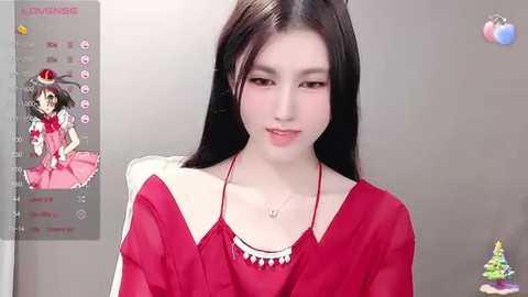 Media: Video of an East Asian woman with long black hair, fair skin, and a slender physique, wearing a red dress, standing against a gray wall. The background includes a screen displaying a character from \"Touhou Project\" and a small Christmas tree.