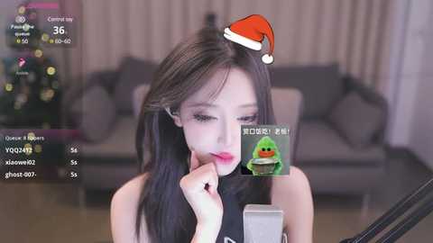 Media: Video of a young East Asian woman with long black hair, wearing a red Santa hat, in a modern living room with a Christmas tree. She is holding a camera.