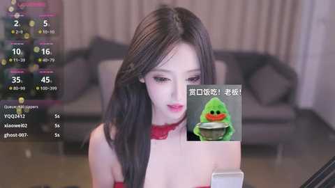 Media: A video of an Asian woman with long black hair, wearing a red dress, using a smartphone, in a modern living room with grey couches.