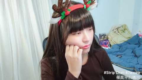 Media: Video of a young Asian woman with long dark hair and red reindeer headband, resting her cheek on her hand, wearing a brown sweater. Background features a messy room with a bed and scattered clothes. Text reads \"#5rip Cutie Pawawa.\