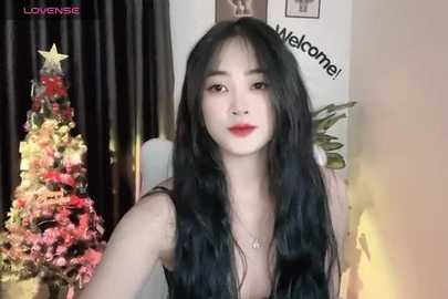 Media: A video of an East Asian woman with long black hair, wearing a sleeveless black dress, standing beside a decorated Christmas tree.