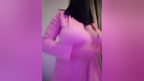 Media: A blurry, low-quality video of a woman with long black hair, wearing a pink sweater, partially obscuring her breasts, standing indoors.