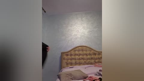 Media: Video of a dimly lit bedroom with a tufted headboard, a messy bed with pink and purple bedding, and a person with long dark hair partially obscured by the frame.