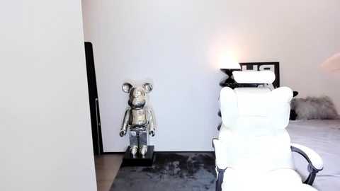 Media: Video of a minimalist room with a silver robot statue, white leather chair, and a cozy, plush rug, featuring a warm, ambient light.