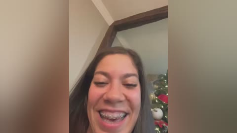 Media: Video of a smiling woman with braces, standing in a corner with a Christmas tree in the background.