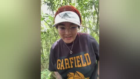 Media: A video of a young woman with glasses, wearing a red visor and a dark \"Carolina\" t-shirt, standing in a lush green forest.