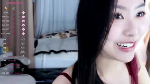 Media: A video of an East Asian woman with long black hair, smiling, wearing a red top, in a bedroom with a bed and curtains.