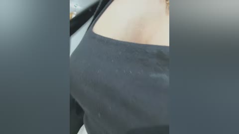 Media: Video of a close-up of a woman's chest in a black tank top, with a blurred background, highlighting her cleavage.