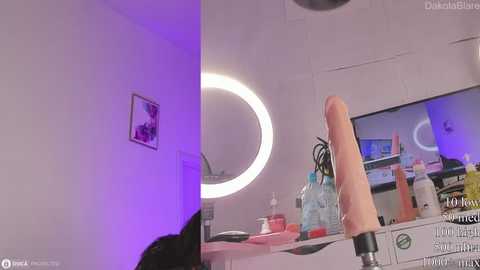 Media: A video of a woman using a dildo in a brightly lit, minimalist room with a round mirror, framed by a purple light.