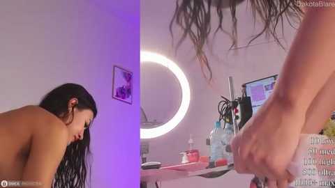 Media: Video of a young woman with long, black hair, topless, in a dimly lit room, with a mirror, makeup brushes, and a framed picture on the wall.