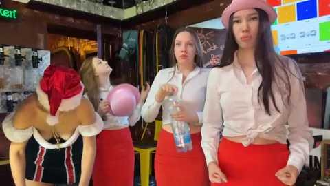 Media: Video of four young women in a bar, one in a Santa outfit, two in white tops and red skirts, and one in a pink hat and skirt, all holding drinks.