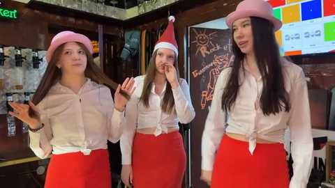 Media: Video of three young women in a cozy, brightly lit cafe. They wear red skirts, white tops, and pink hats, smiling and chatting. Background features a chalkboard with \"Breakfast\" and a sun illustration.