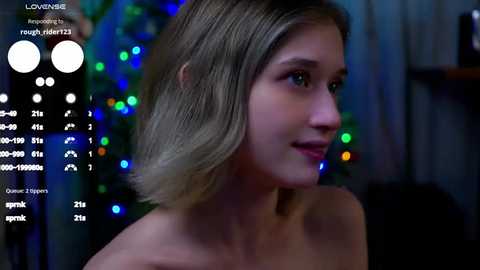 Media: A video of a fair-skinned woman with shoulder-length, straight, blonde hair, smiling slightly, set against a blurred background with colorful LED lights and a digital interface displaying her vital signs.