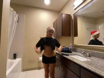 Media: Video of a young woman with a red hat and black top, standing in a modern bathroom with a granite countertop, mirror, and white bathtub.