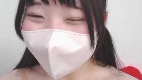 Media: Video of an East Asian woman with long black hair, wearing a white medical mask, eyes closed, against a plain white background.