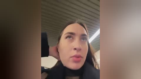 Video of a Caucasian woman with fair skin, long brown hair, and large brown eyes, looking up with a pensive expression. Background features a modern, industrial ceiling with metal beams.