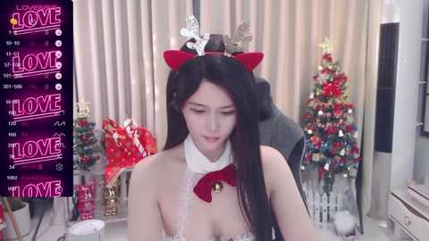 Media: Video of a young Asian woman with long black hair wearing a red and white Santa costume, sitting at a festive, decorated table with a Christmas tree in the background.