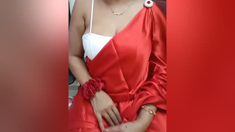 Media: A video shows a woman in a red satin gown, exposing a white bra, wearing a gold bracelet and a red scrunchie, against a red backdrop.