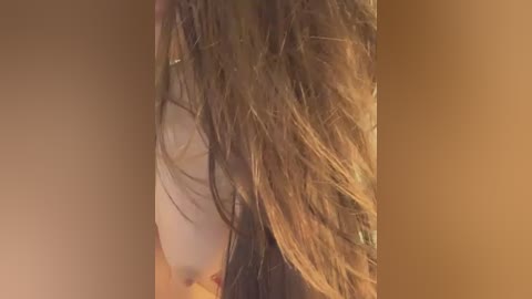 Media: Video of a woman with wet, brown hair cascading down her left side, highlighting her partially visible, fair-skinned breast. The background is a warm, brown gradient, adding a cozy, intimate atmosphere.