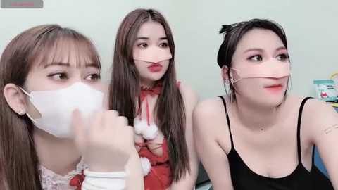 Media: Video of three young Asian women, wearing face masks and festive Santa outfits, indoors with a plain background.