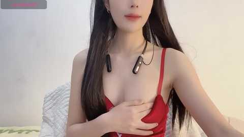 Media: Video of a slender Asian woman with long, straight black hair, wearing a red bra, with headphones on, in a bedroom with white walls.